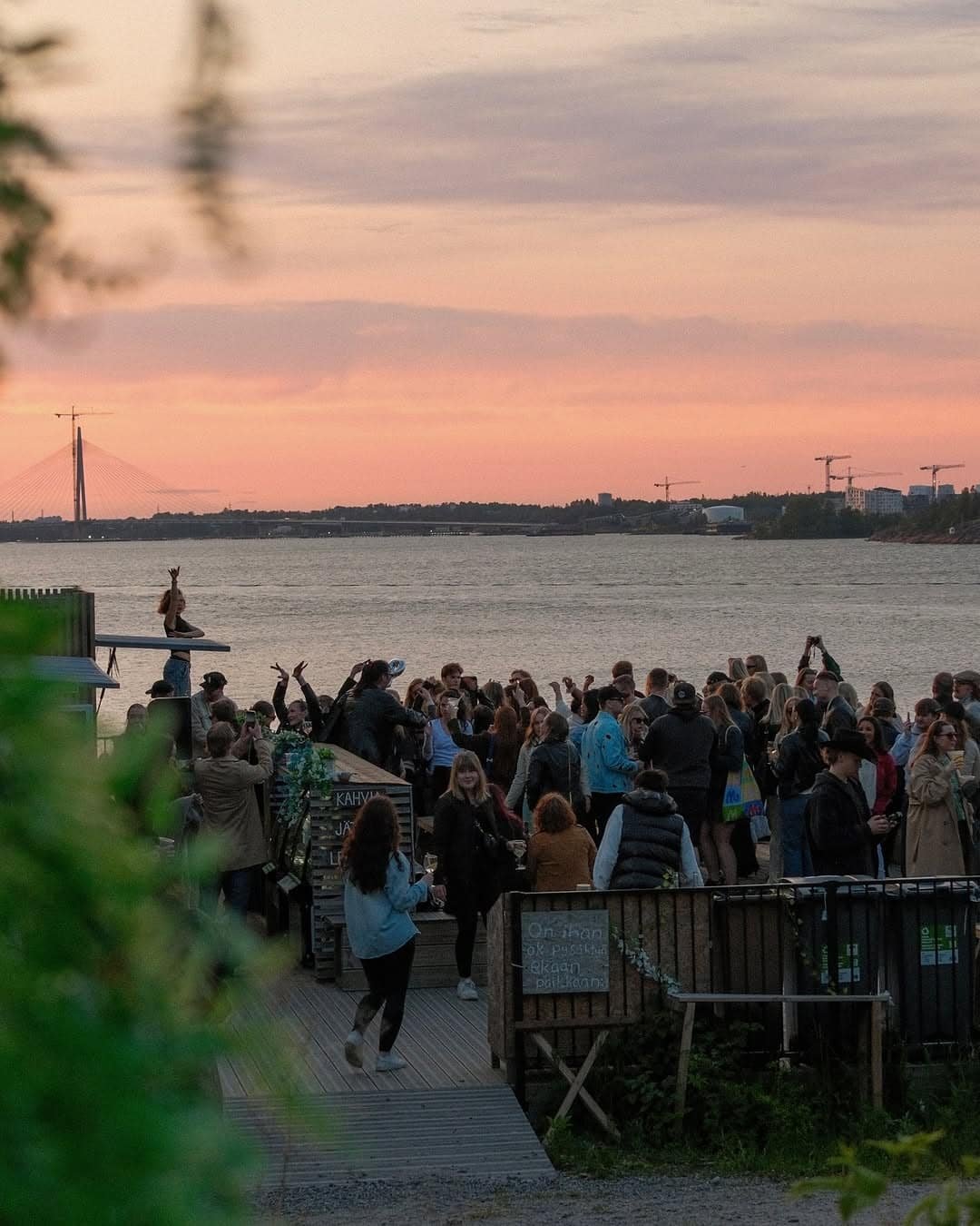 Sunset crowd on the IISI Vallisaari terrace, with the sea and Helsinki skyline in the background